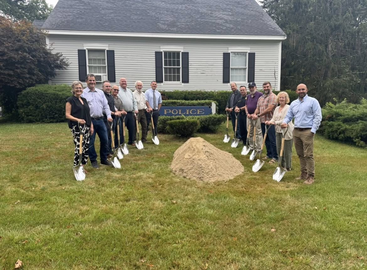 People holding shiny chrome shovels around a mound of dirt in front of the Police Station